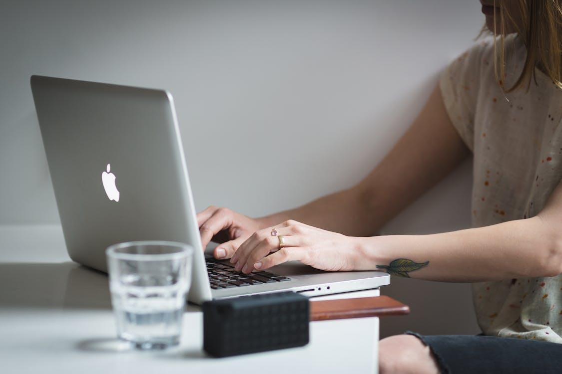 Free Woman Using Silver Macbook Near Shot Glass on Table Stock Photo